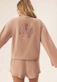 Jasnoróżowy, krótki sweatshirt z długimi rękawami i grafiką muszli na plecach. Połączony z dopasowanymi szortami z miękkiego materiału.