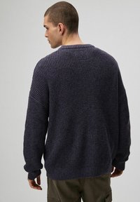 Gruby sweter z dzianiny w ciemnym granacie o teksturowanej powierzchni, z opuszczonymi ramionami oraz ściągaczami przy mankietach i dolnym brzegu. Widok z tyłu, bez widocznych oznaczeń.