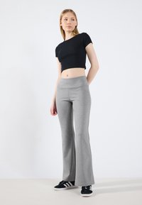 Svart croppet t-skjorte med korte ermer, sammen med grå flagrende joggebukser. Outfitten kompletteres av svarte sko med hvite striper.