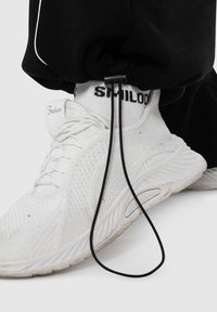 Hvide mesh sneakers med tekstureret overflade, prydet med sorte snøre detaljer og en sort snor. Båret med en hvid, mønstret sok.