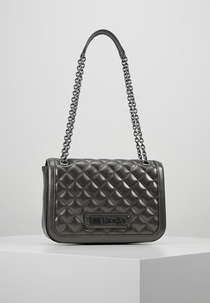 Sac d’épaule matelassé noir avec bandoulière chaîne et plaque logo "LOVE MOSCHINO" sur le devant, exposé sur un socle blanc.