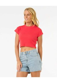Top corto a maniche corte rosso a coste abbinato a pantaloni shorts in denim azzurro chiaro. L'outfit presenta un design aderente e un look casual.