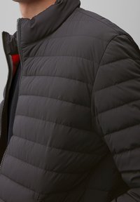 Giacca a vento nera con collo alto, caratterizzata da una texture trapuntata e chiusura con zip. L'interno foderato aggiunge dettaglio e calore.