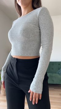 Top cropped de mangas longas cinza claro com um design ajustado e punhos com buraco para os polegares, combinado com calças pretas de cintura alta.