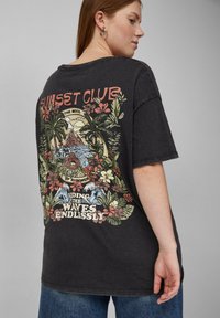 Zwart oversized T-shirt met een kleurraf tropisch ontwerp op de achterkant met tekst. Korte mouwen, ronde hals en een relaxte pasvorm.