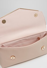 Béžová syntetická kabelka s hladkou strukturou, zlatými kovovými doplňky a jemně růžovým vnitřkem, který obsahuje kapsu na zip a zapínání na patentku.