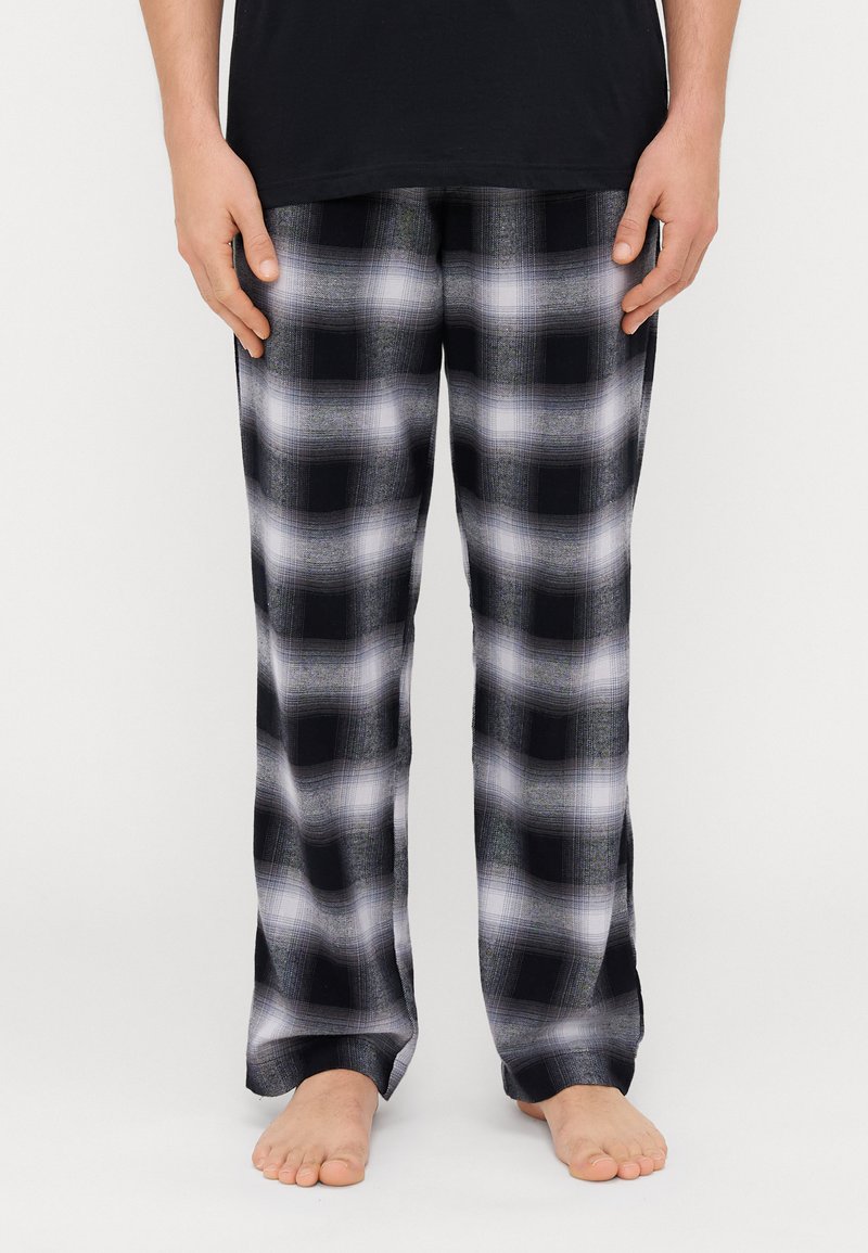 Pantalons de pyjama à carreaux noir et blanc avec une texture douce, présentant une coupe ample et des jambes droites, portés pieds nus.