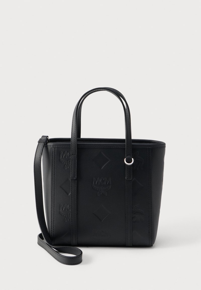 Sac cabas en cuir noir avec logos MCM embossés, double poignée et bandoulière amovible sur fond blanc uni.