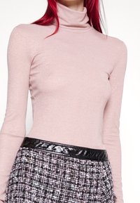 Helles rosa Rollkragensweater aus einem weichen, schimmernden Stoff. Langer Ärmel, glatte Textur, kombiniert mit einem schwarzen Lacklederbund.