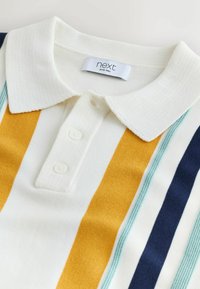 Polo blanc avec des rayures verticales moutarde, sarcelle et marine, deux boutons blancs et une étiquette de marque "next" à l'intérieur du col.