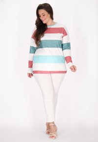 Top cu maneci lungi în dungi, de culoare roșie, teal, alb și albastru, confecționat dintr-un material moale; asortat cu pantaloni slim-fit albi și sandale cu toc bloc bej.