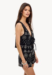 Top sans manches noir avec un décolleté en V profond et un lien frontal, orné de clous argentés de différentes formes, associé à un short assorti.