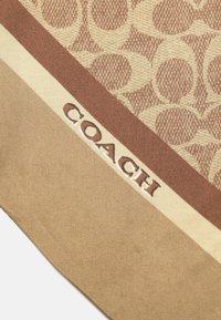 Bufanda de color marrón con un patrón que presenta un logo de Coach en una franja beige en contraste, confeccionada en una tela suave con una textura lisa.