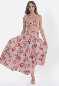 Abito floreale a due pezzi che presenta un crop top aderente con un frontale attorcigliato e una gonna fluttuante a strati nei toni del rosa, bianco e verde.