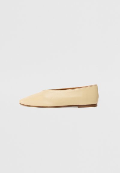 Ballerines en cuir beige avec un bout pointu, semelle plate et détails de couture minimalistes, présentant une texture lisse et un design simple.