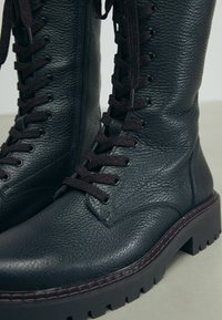 Stivaletti neri in pelle con lacci, caratterizzati da una finitura testurizzata, con lacci color bordeaux e una suola robusta, dotati di una cerniera laterale per una facile vestibilità.