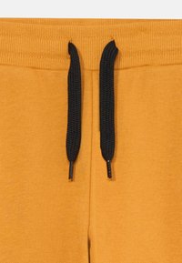 Mosterdgele joggingbroek met een geribbelde waistband, voorzien van zwarte trekkoorden en een zachte, gestructureerde stof.