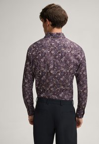 Langärmliges Hemd in Dunkellila mit floralem Muster in sanften Farben. Klassischer Kragen und Knopfdetails. Kombiniert mit dunkler Hose.