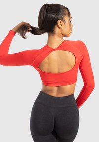 Rode cropped top met lange mouwen en een grote uitsnede op de rug. Gecombineerd met zwarte high-waisted leggings, die de taille en rug accentueren.