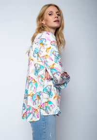 Bunte Bluse mit Elefantenmustern in Blau, Pink und Orange. Seidenmaterial, lockerer Schnitt, lange Ärmel und seitliche Schlitze für Komfort.