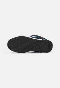 Suola in gomma nera con grip testurizzato, caratterizzata da accenti blu e rossi. Progettata per la stabilità con una forma curvata ed ergonomica.