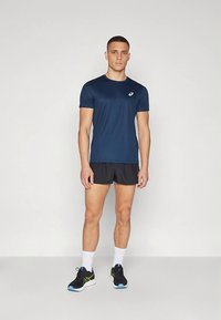 Maglietta sportiva a maniche corte color navy, abbinata a pantaloncini neri. Il modello indossa scarpe da corsa nere con accenti blu e verdi e calzini bianchi.