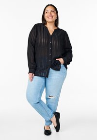 Schwarz gestreiftes Hemd mit Knopfleiste und V-Ausschnitt, langen Ärmeln und lockerer Passform, kombiniert mit hellblauen, ausgefransten Jeans und schwarzen Ballerinas.