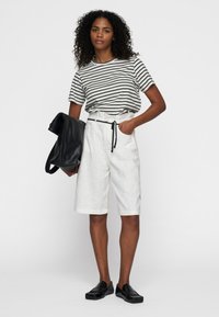 Camiseta de rayas en blanco y negro, pantalones cortos blancos de tiro alto con cordón y bolso negro. La modelo lleva zapatillas negras sin cordones.