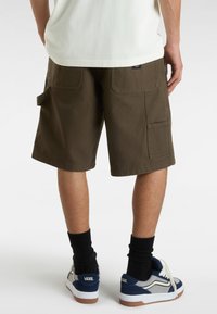 Cargo-Shorts in dunkelolivgrün, mit zwei Seitentaschen und einer Gesäßtasche, aus strapazierfähigem Stoff. Kombiniert mit marineblauen Sneakers und schwarzen Socken.