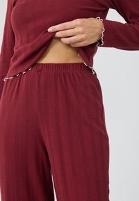 Burgundy ribbad loungedräkt som består av en långärmad topp med vågiga mudd och midja, kompletterad av elastiska byxor.