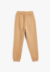 Pantalones deportivos color beige hechos de material suave, con cintura elástica, tobillos ajustados y un corte relajado.