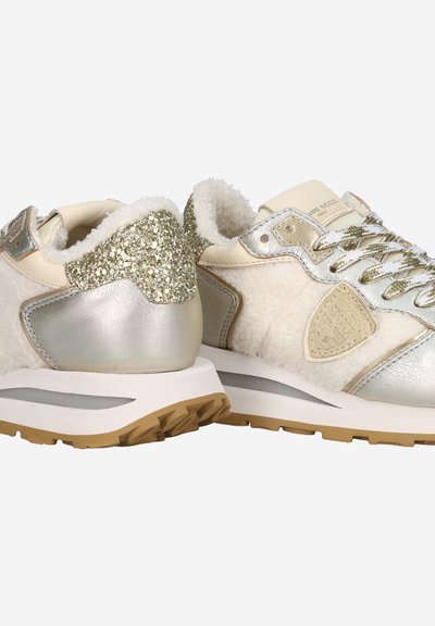 Beige athletic shoes with textured fur and metallic silver accents. Glittery heel detail and a white midsole with a gum outsole.