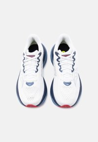 Ζευγάρι λευκά αθλητικά παπούτσια Saucony με μπλε σκούρες και κόκκινες λεπτομέρειες, σε θέα από πάνω, σε ανοιχτό γκρι φόντο.