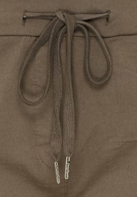 Brun snøre med en tæt vævet tekstur og sølvmetalliske spidser, fastgjort til et beklædningsstykke lavet af blødt, holdbart stof.