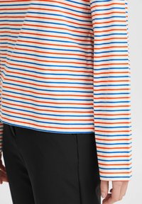 Chemise à manches longues avec des rayures horizontales rouges, bleues et blanches sur un fond clair; fabriquée en tissu doux et lisse avec une coupe décontractée.