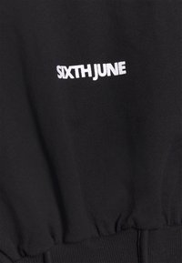 Sudadera negra con texto bordado blanco "SIXTH JUNE". El material es suave; el diseño incluye puños y cinturilla acanalados para una forma ajustada.