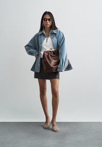 Veste en jean, haut blanc texturé, pochette en cuir marron, mini jupe noire, sandales beiges à fines lanières et lunettes de soleil. Design minimaliste.