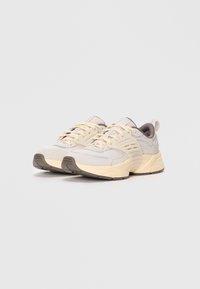 Para beżowych i kremowych sneakersów sportowych z siateczkowej tkaniny, z wyściółką w podeszwie i sznurowadłami, umieszczonych na jednolitym białym tle.