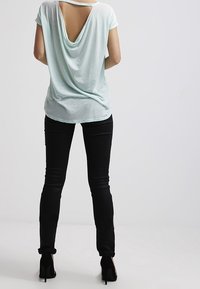 Lysblå draperet top med åben ryg; parret med sorte skinny jeans og høje hæle. Blødt, åndbart stof med en afslappet pasform.