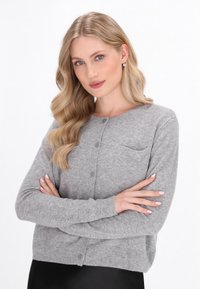 Harmaa neulecardigan, jossa on pyöreä pääntie, napitus edessä ja yksi rintatasku. Varustettu ribbineuloksella käsivarsien ja helman kohdalla, jotta se istuu hyvin.