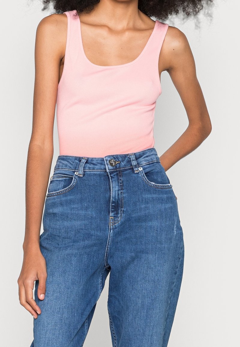 Débardeur rose côtelé associé à un jean en denim bleu taille haute, avec une coupe droite, des coutures visibles et des poches avant.