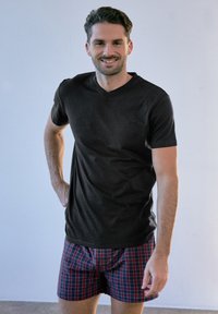 Černé tričko s véčkovým výstřihem vyrobené z hladkého materiálu, spárované s červenými kostkovanými trenýrkami, které mají volný střih a jemné detaily v šití.