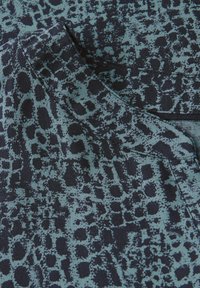 Blue and black patterned fabric with a textured, animal print design. Smooth texture and close-up view of the cloth's edge and seam.