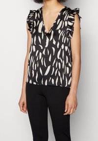 Black top featuring a deep V-neck and short ruffled sleeves. It has a bold white brushstroke pattern throughout.