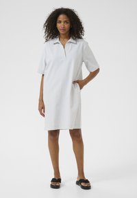 Robe en coton rayée avec un col, des manches courtes et des poches latérales. La robe est bleu clair avec des rayures blanches et possède une coupe droite.