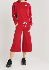 Röd Nike-tröja med matchande korta byxor som har vita sidostänger och logotyp, tillverkad av mjukt tyg med en avslappnad passform.