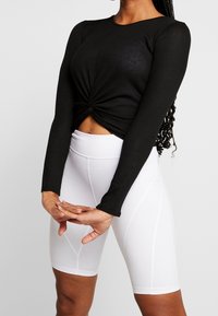 Svart, ribbade långärmad topp med knuten front, kombinerad med högmidjade vita leggings med panelstickningsdetaljer.