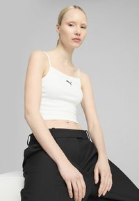 Hvid ribbet crop top med justerbare stropper, med et lille sort Puma-logo på brystet. Sammen med højtrækkende sorte bukser.