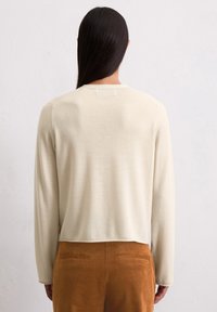 Cremefarbenes, langärmliges Sweatshirt mit einem kurzen Design und glatter Textur, kombiniert mit rostfarbener Cordhose mit Gesäßtaschen.