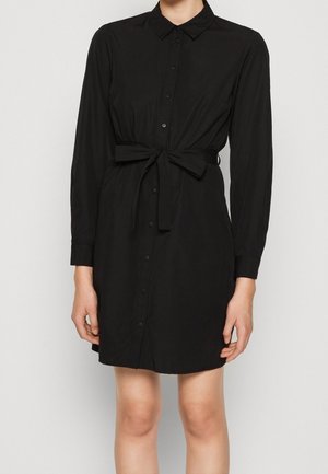 Schwarzes Hemdkleid mit langen Ärmeln, Taillendetail mit Bindeband und Kragen. Glatte Stofftextur, knielang, dezenter Glanz.